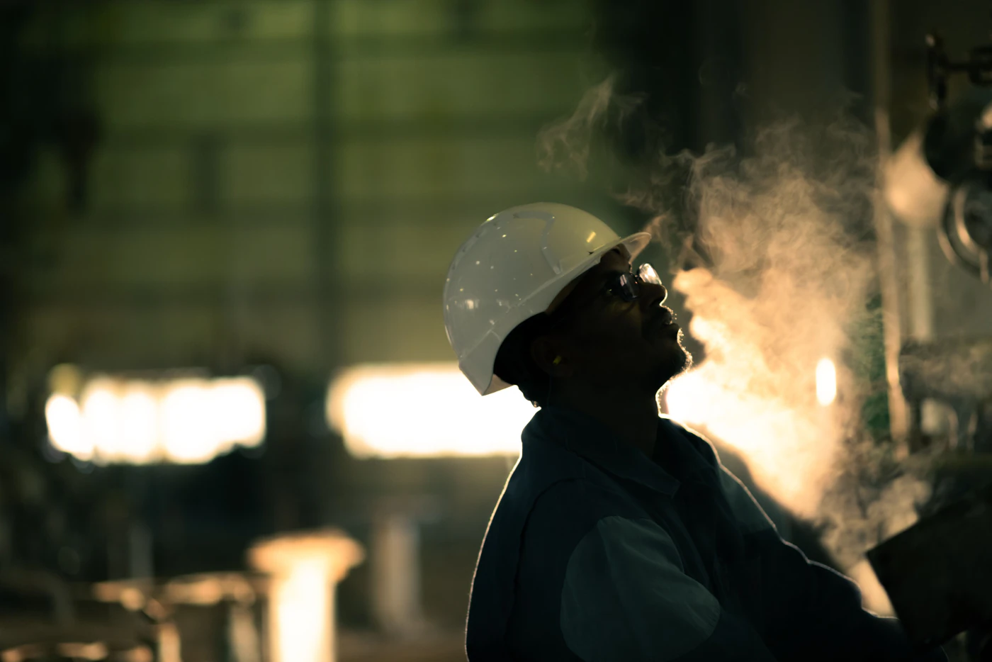 A worker in a hard hat silhouetted against furnace glow